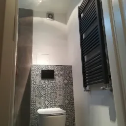 Nowoczesna toaleta z czarno-białymi płytkami dekoracyjnymi, wiszącą miską WC i czarnym grzejnikiem drabinkowym, oświetlona punktowo