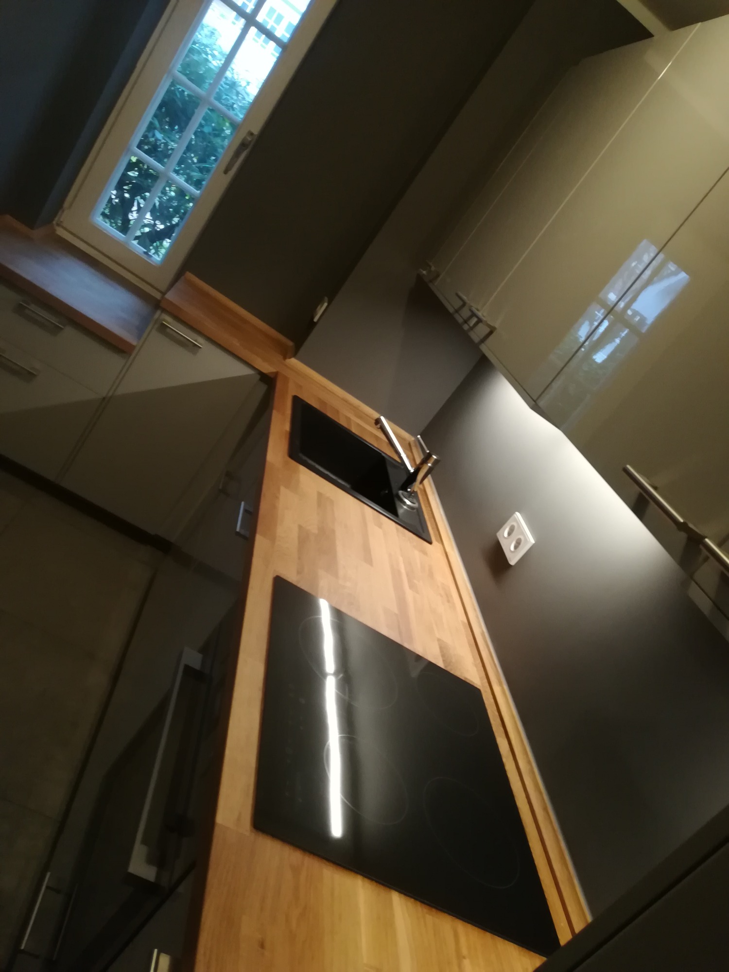 Nowoczesna kuchnia z drewnianym blatem, czarną płytą indukcyjną i zlewozmywakiem, widok z dołu podkreśla minimalistyczny design i jasne wnętrze z oknem.