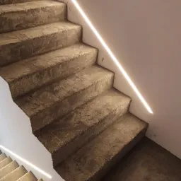 Betonowe schody z wbudowanym oświetleniem LED wzdłuż ściany, widok z dołu, minimalistyczny design.