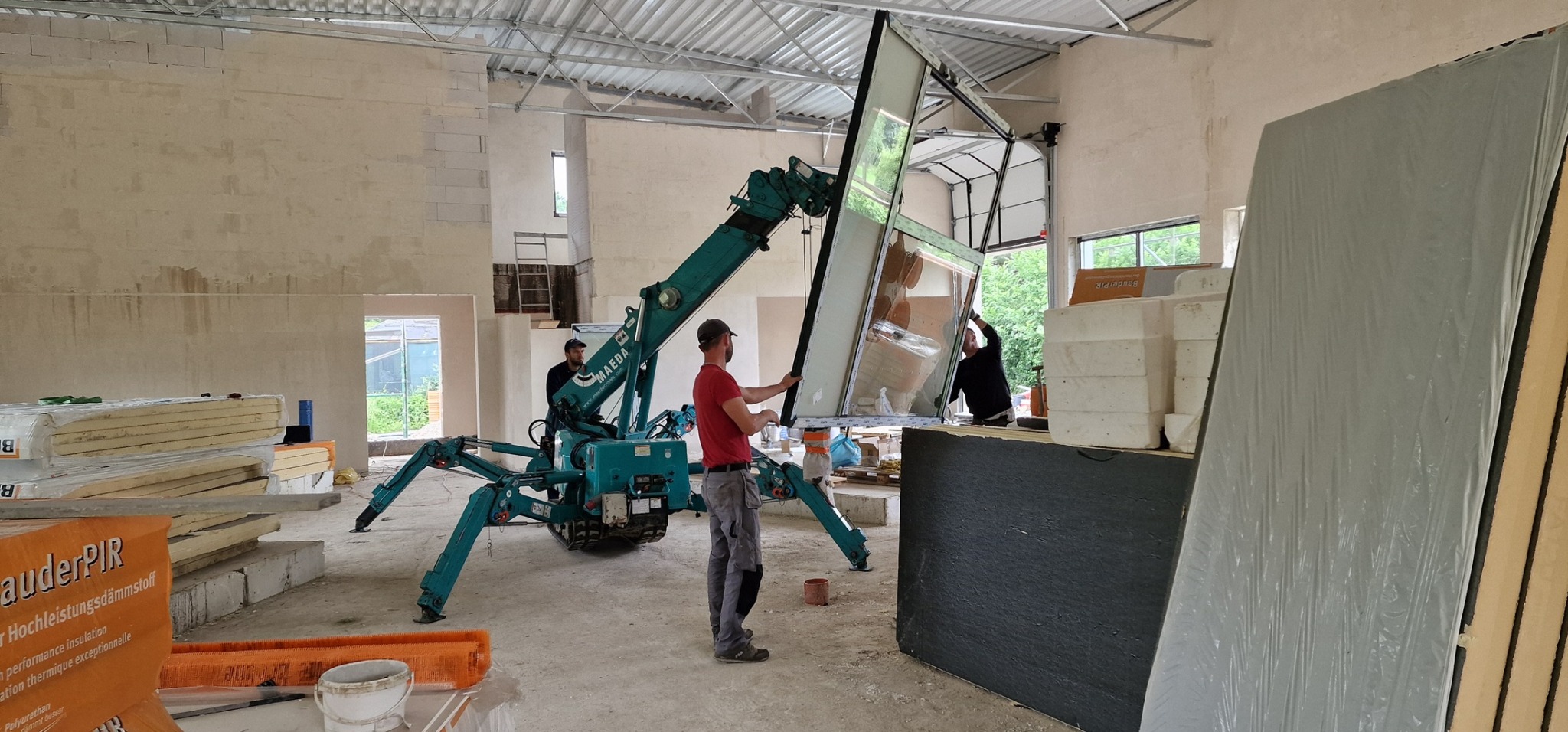 Montaż dużego okna z użyciem specjalistycznego dźwigu w surowym wnętrzu budynku.