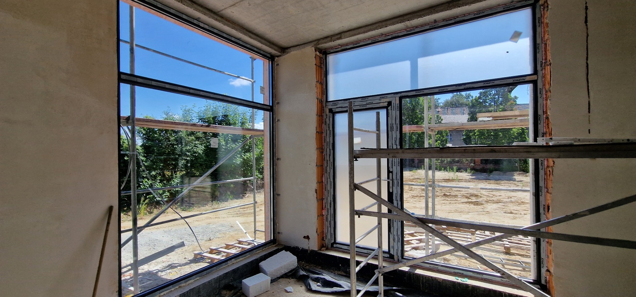 Montaż okien w surowym stanie budynku, widoczne rusztowania i niezabezpieczone ściany.