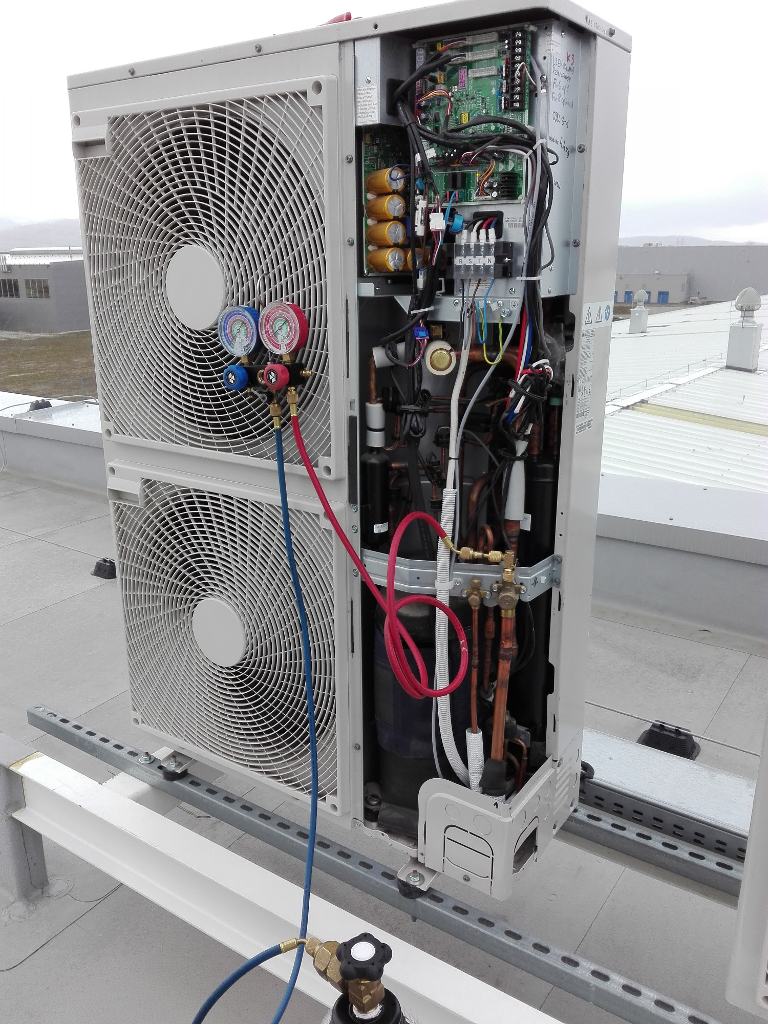 Serwis klimatyzacji w Dzierżoniowie: klimatyzator z otwartą obudową, podłączone manometry i butla z gazem chłodniczym na dachu budynku przemysłowego.