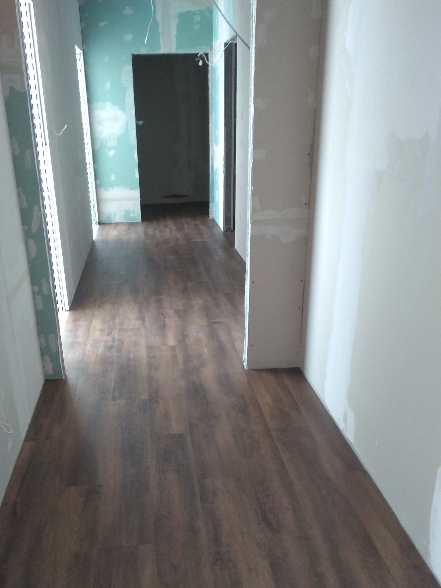 Nowa, ciemnobrązowa podłoga panelowa w korytarzu w trakcie remontu, ściany w stanie surowym, widoczne płyty gipsowo-kartonowe.