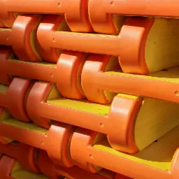 Stos belek szalunkowych z żółtego drewna i pomarańczowymi, plastikowymi wzmocnieniami na końcach, ułożonych równolegle.