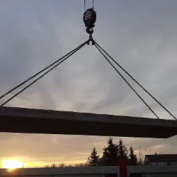 Żelbetowa płyta fundamentowa podnoszona przez dźwig na tle zachodzącego słońca i pochmurnego nieba.