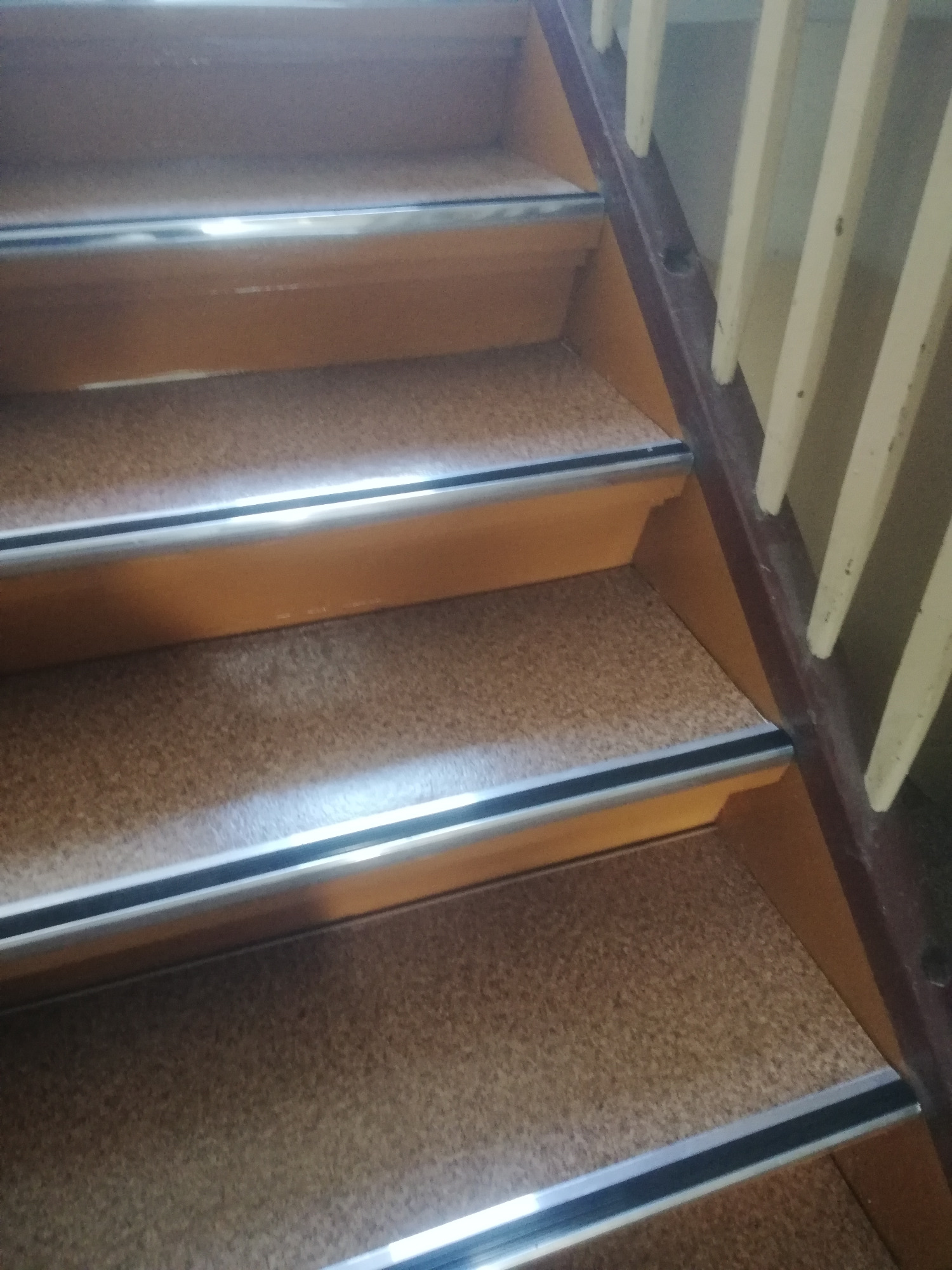 Schody wykończone korkiem z aluminiowymi listwami antypoślizgowymi na krawędziach stopni, widoczne białe barierki schodowe.