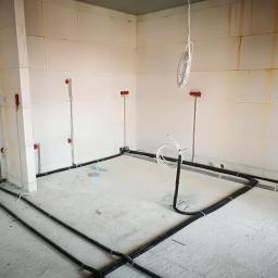 InSE-ET Jarosław Kowalczyk - Wnętrze w trakcie prac instalacyjnych: widoczne kable prowadzone po podłodze i pionowo po ścianach z czerwonymi puszkami instalacyjnymi, ściany z białych bloczków, surowy beton na podłodze.