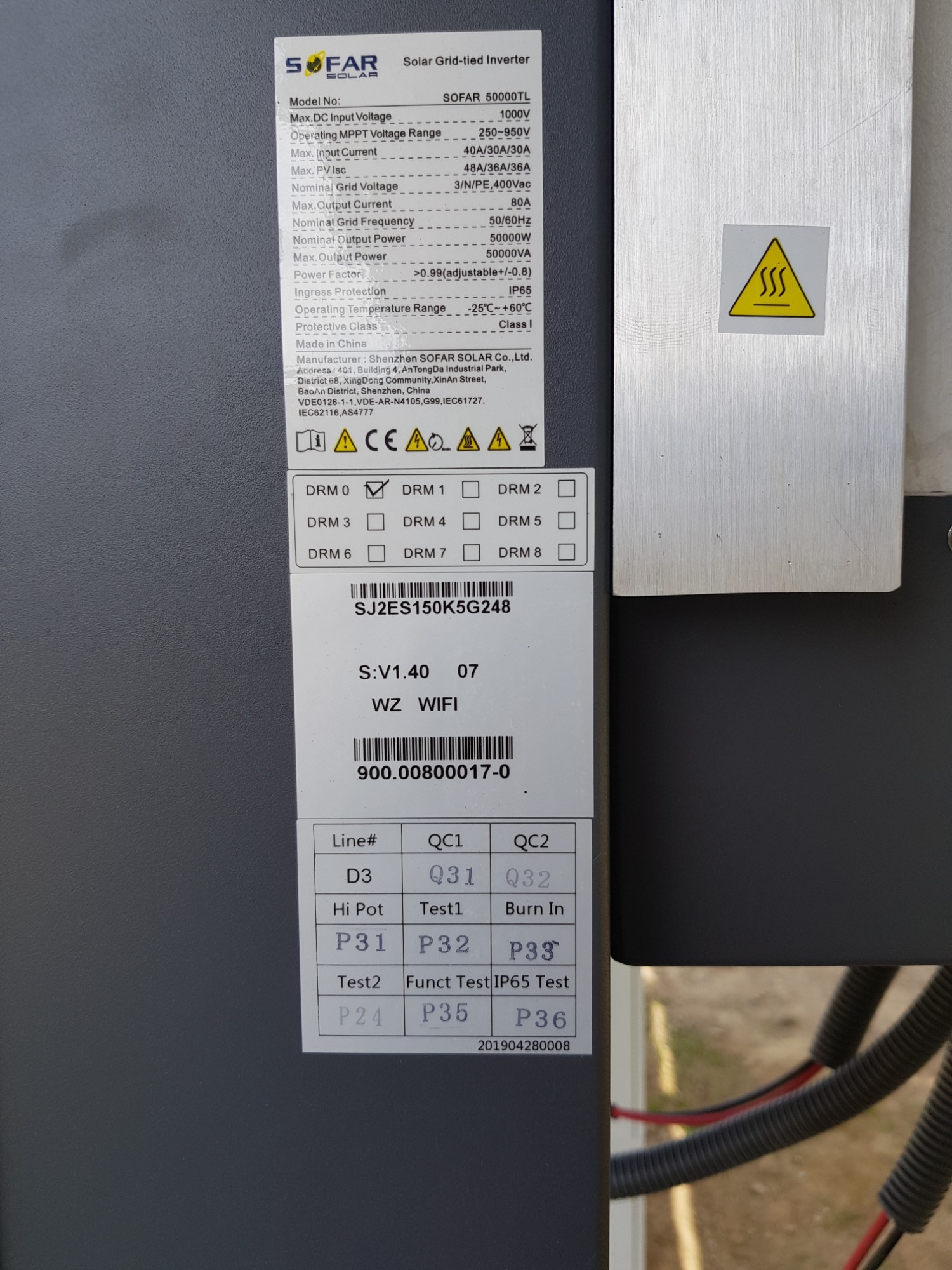 Szczegółowe ujęcie tabliczki znamionowej inwertera SOFAR 50000TL z parametrami technicznymi, numerem seryjnym i kodami testowymi QC, widoczny symbol ostrzegawczy wysokiej temperatury oraz fragment...