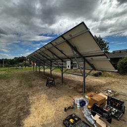 Kopitza Instalacje - Montaż paneli słonecznych na konstrukcji stalowej, widoczne narzędzia i skrzynki narzędziowe na ziemi, pochmurne niebo w tle, etap instalacji.