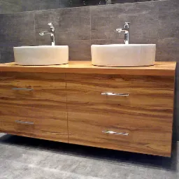 Nowoczesna szafka łazienkowa z drewna o wyraźnym usłojeniu, z dwoma okrągłymi umywalkami nablatowymi i chromowanymi bateriami, na tle szarej ściany wyłożonej płytkami.