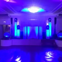 Scena oświetlona intensywnym niebieskim światłem, z kolumnami świetlnymi, reflektorami i białym panelem centralnym, przygotowana na wydarzenie.