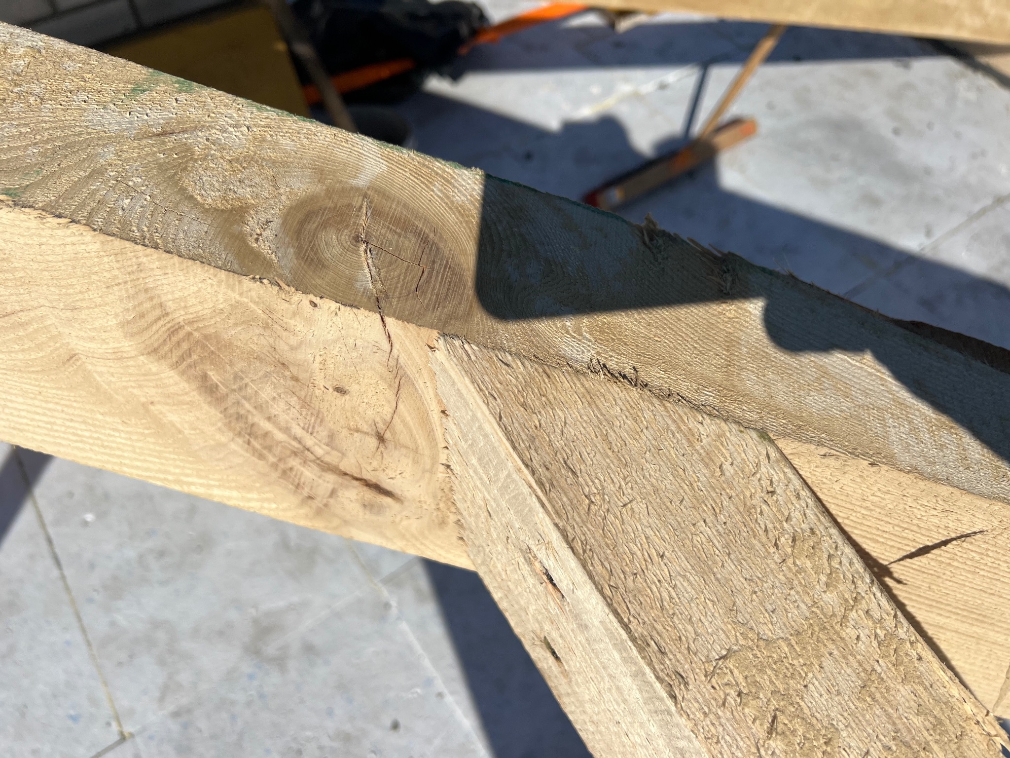 Fragment drewnianej konstrukcji z wyraźnym rysunkiem słojów, prawdopodobnie elementu więźby dachowej, w jasnym, naturalnym oświetleniu.