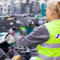 Pracownica w kamizelce odblaskowej z logo Seifert skanuje detektor z użyciem terminala mobilnego w magazynie w Mysłowicach, widoczne elementy w różnych kolorach i kształtach.