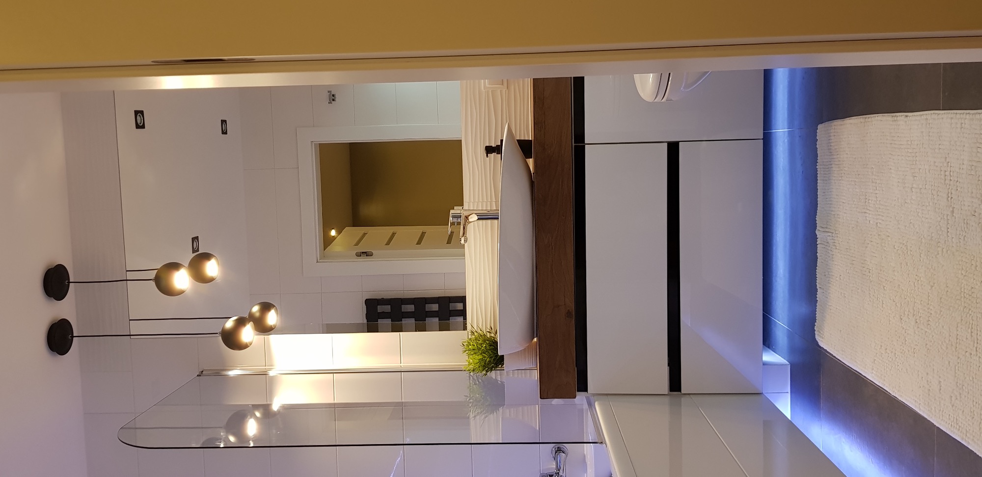 Nowoczesna łazienka z podświetleniem LED, minimalistyczną armaturą, wiszącą szafką z drewnianymi akcentami i dekoracyjnymi lampami kulami.