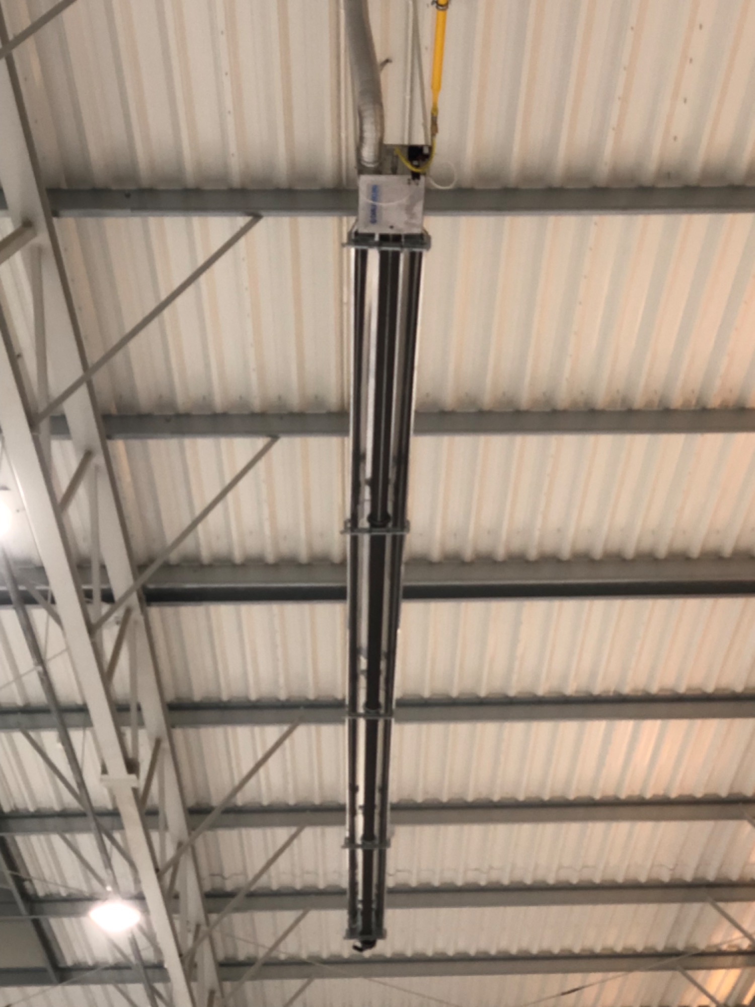 Promiennik gazowy zamontowany pod sufitem hali przemysłowej z blachy trapezowej, widoczne rury doprowadzające gaz oraz elementy mocujące do konstrukcji dachu.