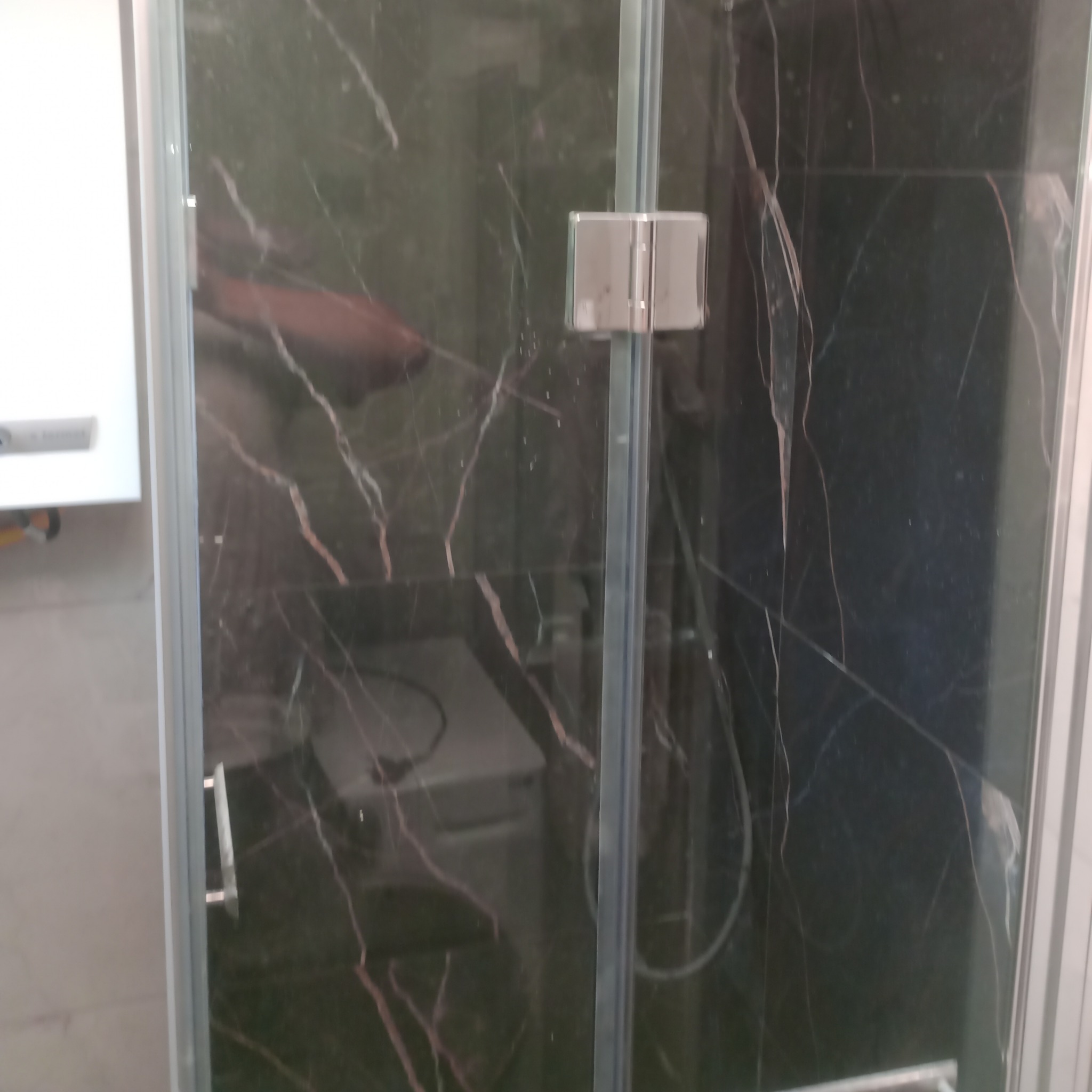 Szklana kabina prysznicowa z czarnymi płytkami imitującymi marmur, srebrne okucia, widoczny fragment białej szafki. Nowoczesny design.