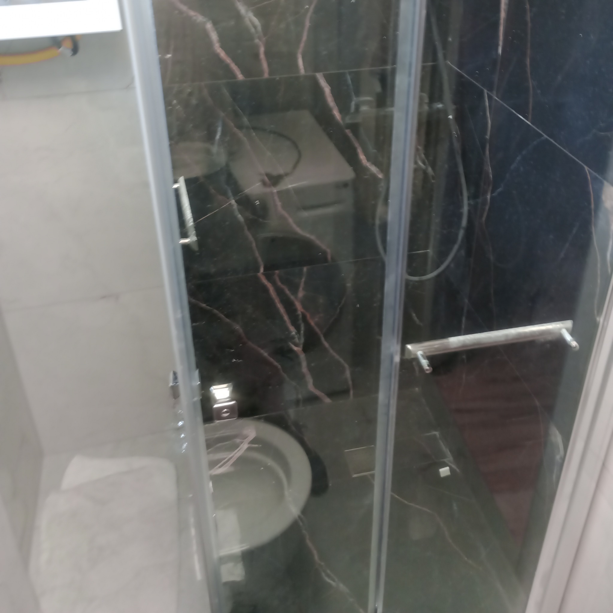 Kabina prysznicowa z czarnymi płytkami imitującymi marmur, widok na toaletę i umywalkę. Elementy chromowane.