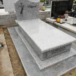 Granitowy nagrobek z inskrypcją 'Filipek' i symbolem krzyża z motywem roślinnym, na cmentarzu, widok z boku.