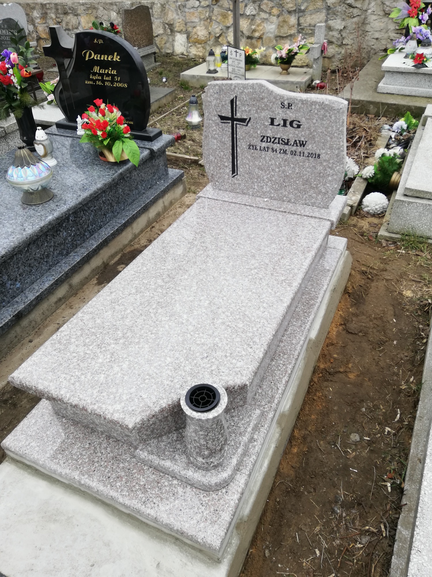 Jasnoszary granitowy nagrobek z krzyżem i imieniem Zdzisław, z wazonem na kwiaty, usytuowany na cmentarzu, widoczny z góry.