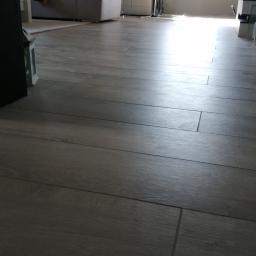 Remonty-Wykonczenia Sobieski - Ułożone szare panele podłogowe w salonie, widoczne fugi i faktura drewna, w tle sofa i stół z krzesłami.