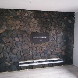 Remonty-Wykonczenia Sobieski - Ściana wykończona kamieniem dekoracyjnym, z przygotowanymi otworami na montaż telewizora i kominka elektrycznego, widoczne metalowe profile montażowe.
