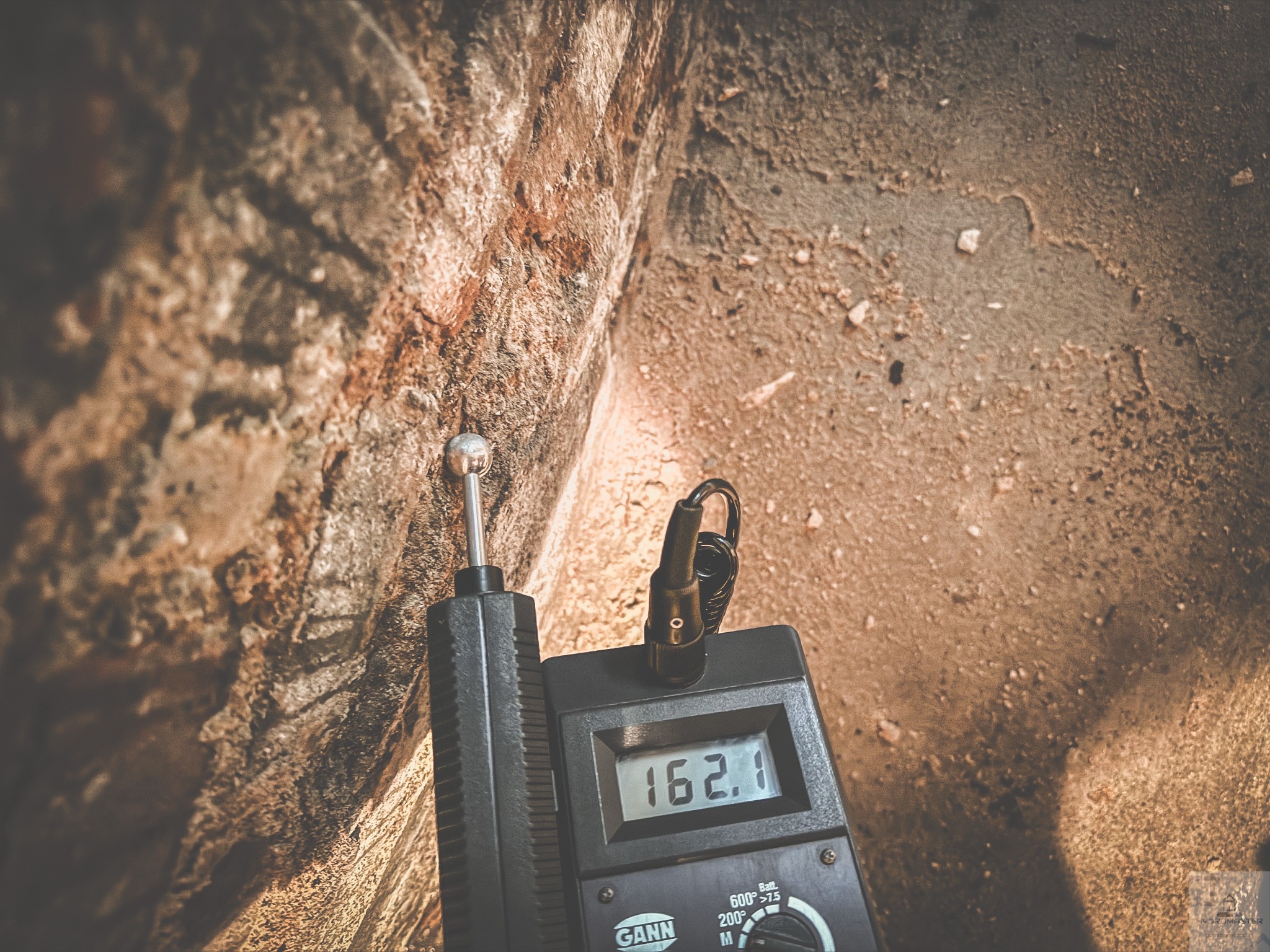 Pomiar wilgotności ściany budynku za pomocą wilgotnościomierza GANN HydroMaster, wskazującego wartość 162.1, w celu diagnostyki problemów z wilgocią.