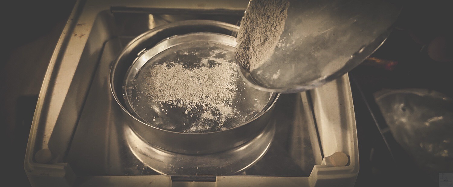 Przesiewanie próbki materiału przez metalowe sito w laboratorium. Analiza składu gruntu lub zaprawy. Badanie jakości materiałów budowlanych.