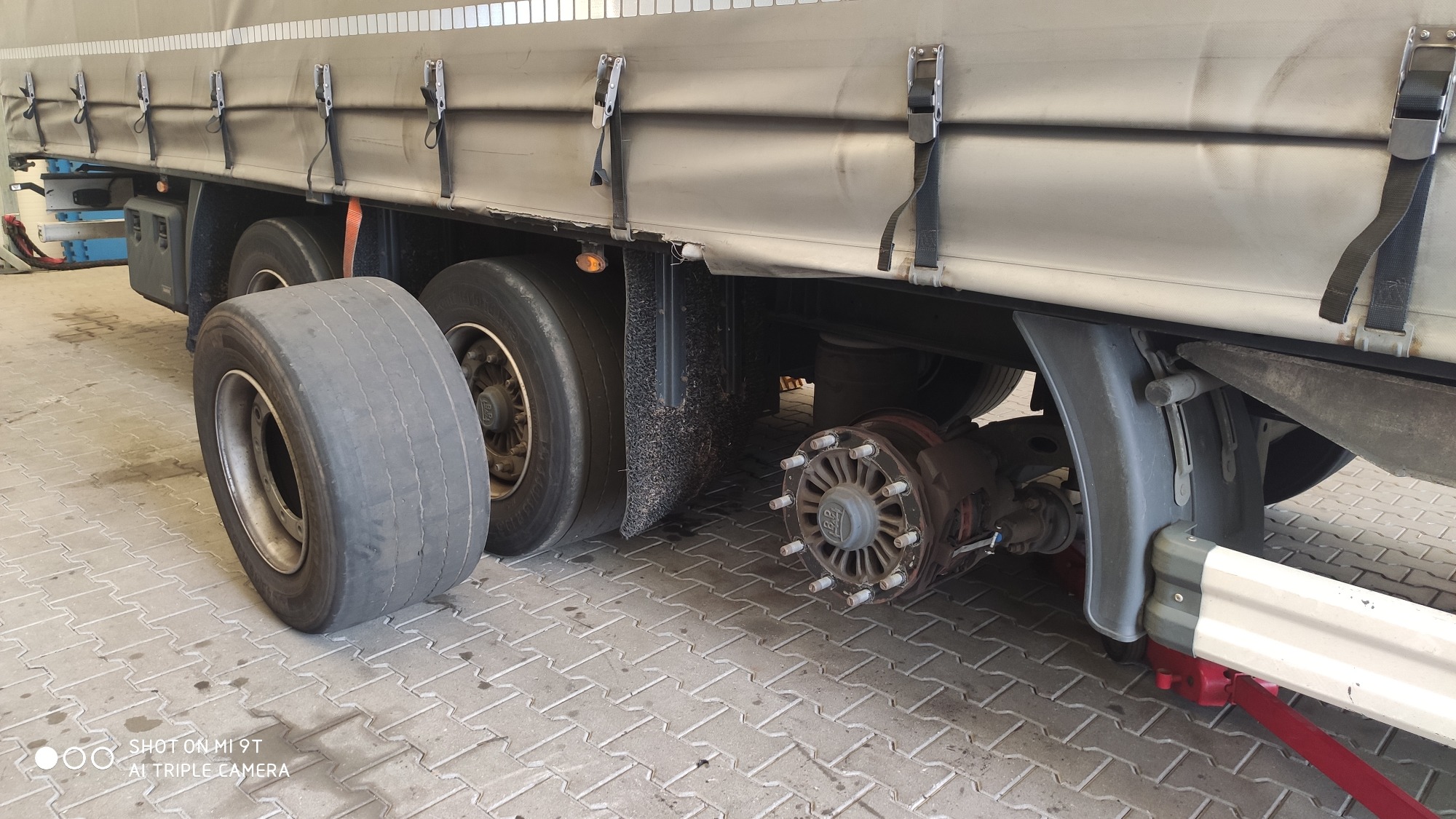 Ciężarówka na podnośniku z odkręconym kołem i zużytą oponą leżącą obok.