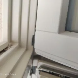 Szczegółowe ujęcie ramy okiennej z widocznymi zabrudzeniami i niedoskonałościami uszczelnienia w rogu. Widoczny mechanizm okienny.