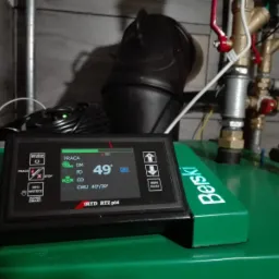 Panel sterowania kotła gazowego marki Berski z wyświetlaczem pokazującym temperaturę 49 stopni Celsjusza, widoczne zawory i rury instalacji, czarny przewód zasilający.