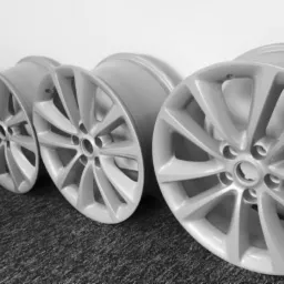 Cztery felgi aluminiowe w kolorze jasnoszarym, ustawione jedna za drugą na ciemnej, teksturowanej powierzchni, prawdopodobnie po procesie czyszczenia lub renowacji.