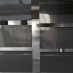 Szare, metalowe elementy balustrady z poziomymi, srebrnymi akcentami, ułożone w rzędach, prawdopodobnie przed montażem.