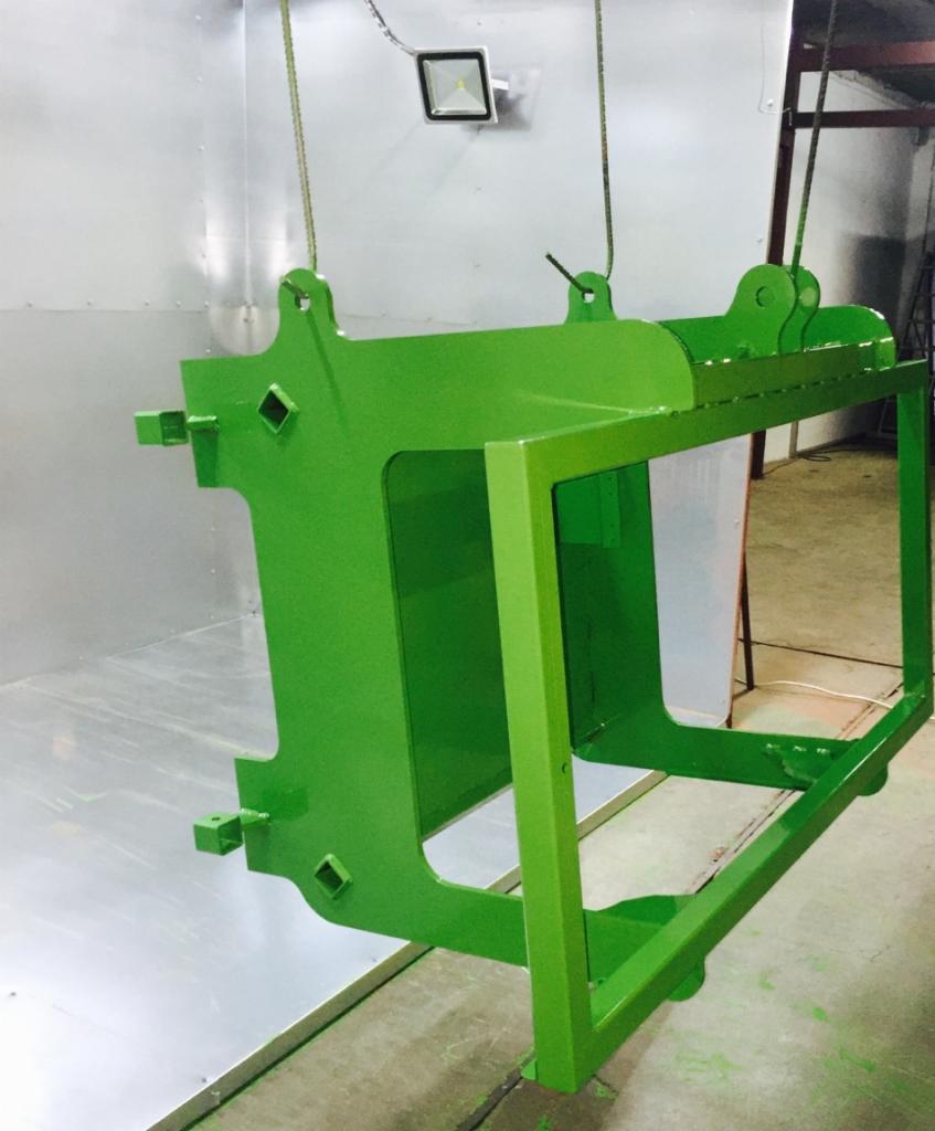 Metalowa konstrukcja pomalowana na jasnozielony kolor, zawieszona w komorze lakierniczej, widoczne detale mocowań i spawów.