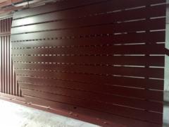 Ciemnobrązowe, poziome panele przesuwnej bramy wjazdowej, częściowo otwarte, z widocznymi elementami konstrukcyjnymi i pionowymi profilami po lewej stronie.