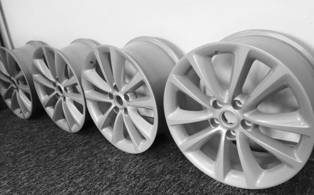 Cztery felgi aluminiowe w kolorze jasnoszarym, ustawione jedna za drugą na ciemnej, teksturowanej powierzchni, prawdopodobnie po procesie czyszczenia lub renowacji.