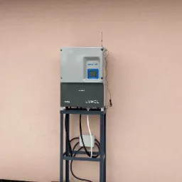 Szaro-czarna obudowa urządzenia pomiarowego Radius Lumel PVSA, umieszczona na metalowym stojaku, z widocznymi kablami, na tle jasnoróżowej ściany budynku i kostki brukowej z resztkami śniegu.