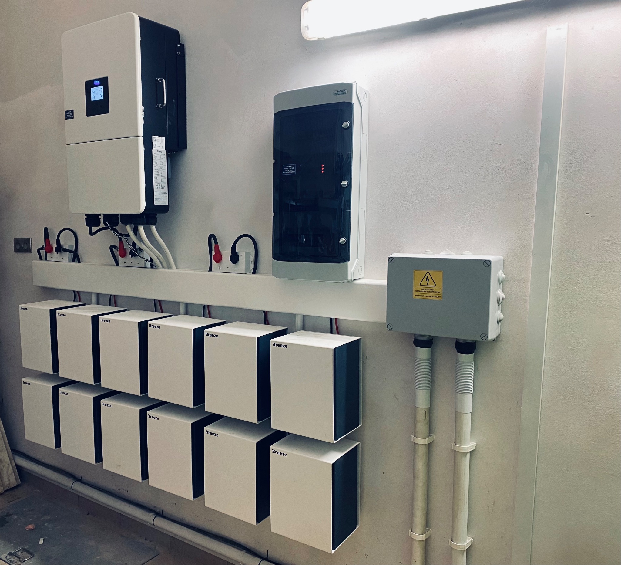 Instalacja magazynu energii Breeze w Serocku, widoczny falownik, zabezpieczenia i szereg modułów bateryjnych zamontowanych na ścianie w pomieszczeniu technicznym.
