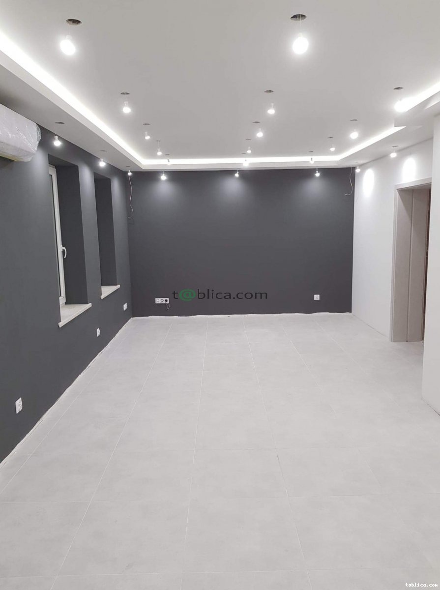 Wnętrze pokoju po remoncie: ściany pomalowane na ciemny szary kolor, jasna podłoga z płytek, sufit z oświetleniem punktowym i listwą LED, widoczne okna z białymi parapetami.