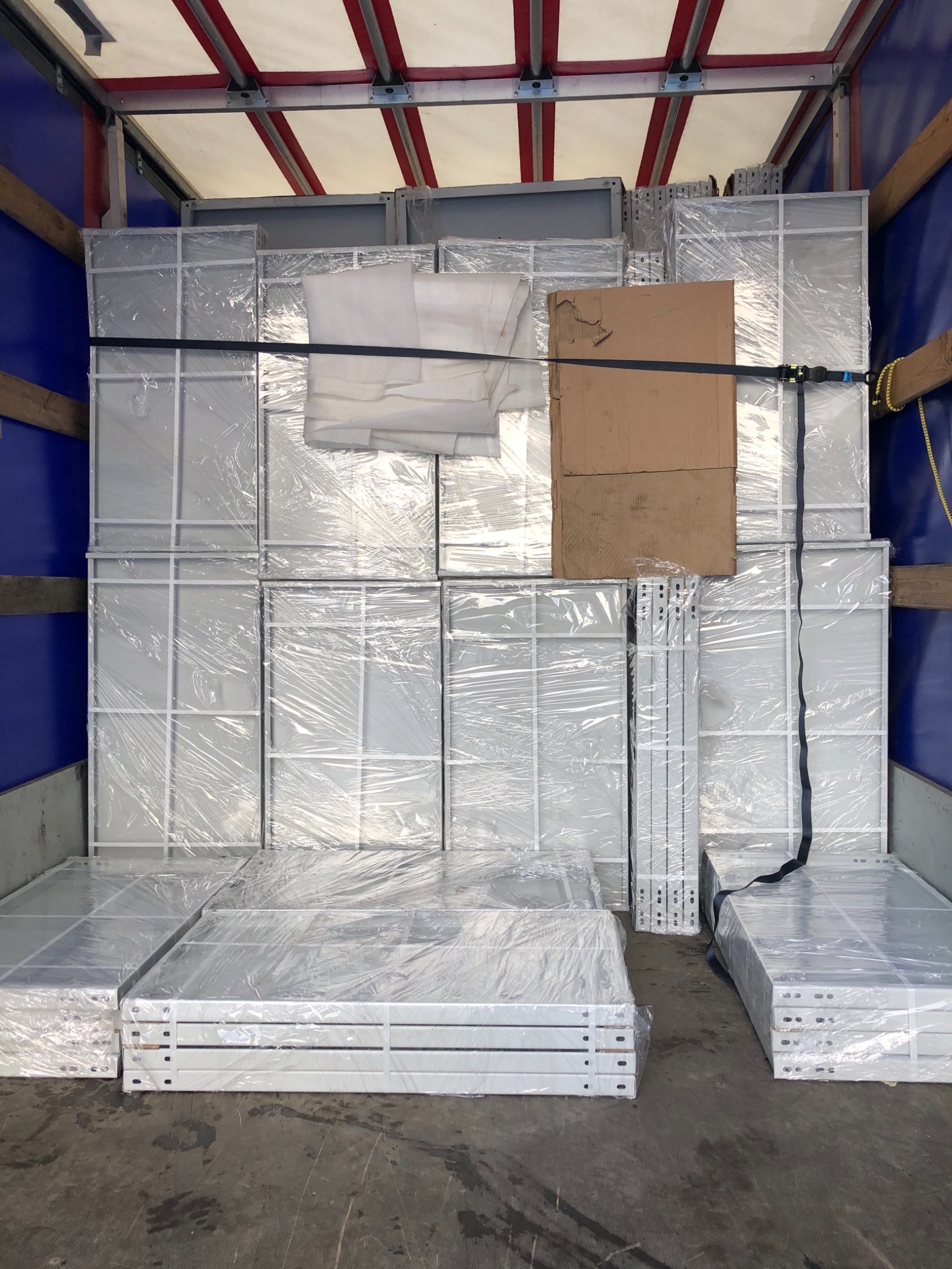 Wnętrze przestrzeni ładunkowej wypełnione paczkami z metalowymi ramami zabezpieczonymi folią i pasami transportowymi.