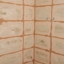 Mirosław Ziemniak - Ściana po nałożeniu warstwy szpachli w kratkę, widoczne dwa otwory na rury, niebieski kij do malowania oparty o ścianę.