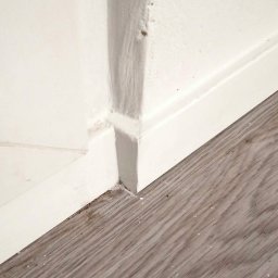 Mirosław Ziemniak - Niedokładne połączenie ściany, listwy przypodłogowej i paneli podłogowych, widoczne niedociągnięcia w szpachlowaniu i malowaniu łączenia.