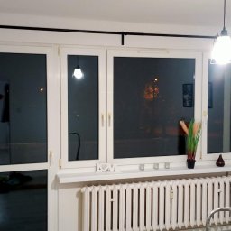 Mirosław Ziemniak - Zabudowany balkon z białymi ramami okiennymi i czarnym karniszem, widok na wnętrze z wiszącą lampą i grzejnikiem pod oknem, dekoracje na parapecie.