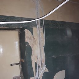 Mirosław Ziemniak - Przygotowanie do malowania: ściana z usuniętą starą farbą, widoczne kable elektryczne i puszka instalacyjna, fragment drzwi z zamkiem.