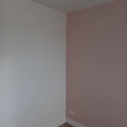 MGS-BUD Remonty i Wykończenia - Pomieszczenie po malowaniu: ściana biała i różowa, listwy przypodłogowe, panele podłogowe. Widoczne gniazdka elektryczne. Minimalistyczny design.
