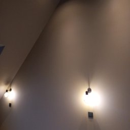 MGS-BUD Remonty i Wykończenia - Poddasze po malowaniu: skośna ściana w odcieniach szarości z zamontowanymi lampami punktowymi i gniazdkami elektrycznymi. Minimalistyczny design.