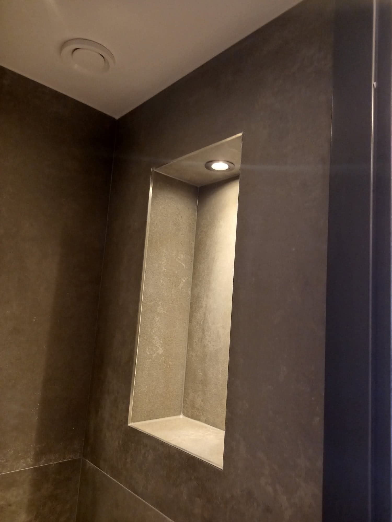 Wnęka z podświetleniem w łazience wykończonej płytkami w odcieniach szarości. Minimalistyczny design, nowoczesne oświetlenie punktowe.