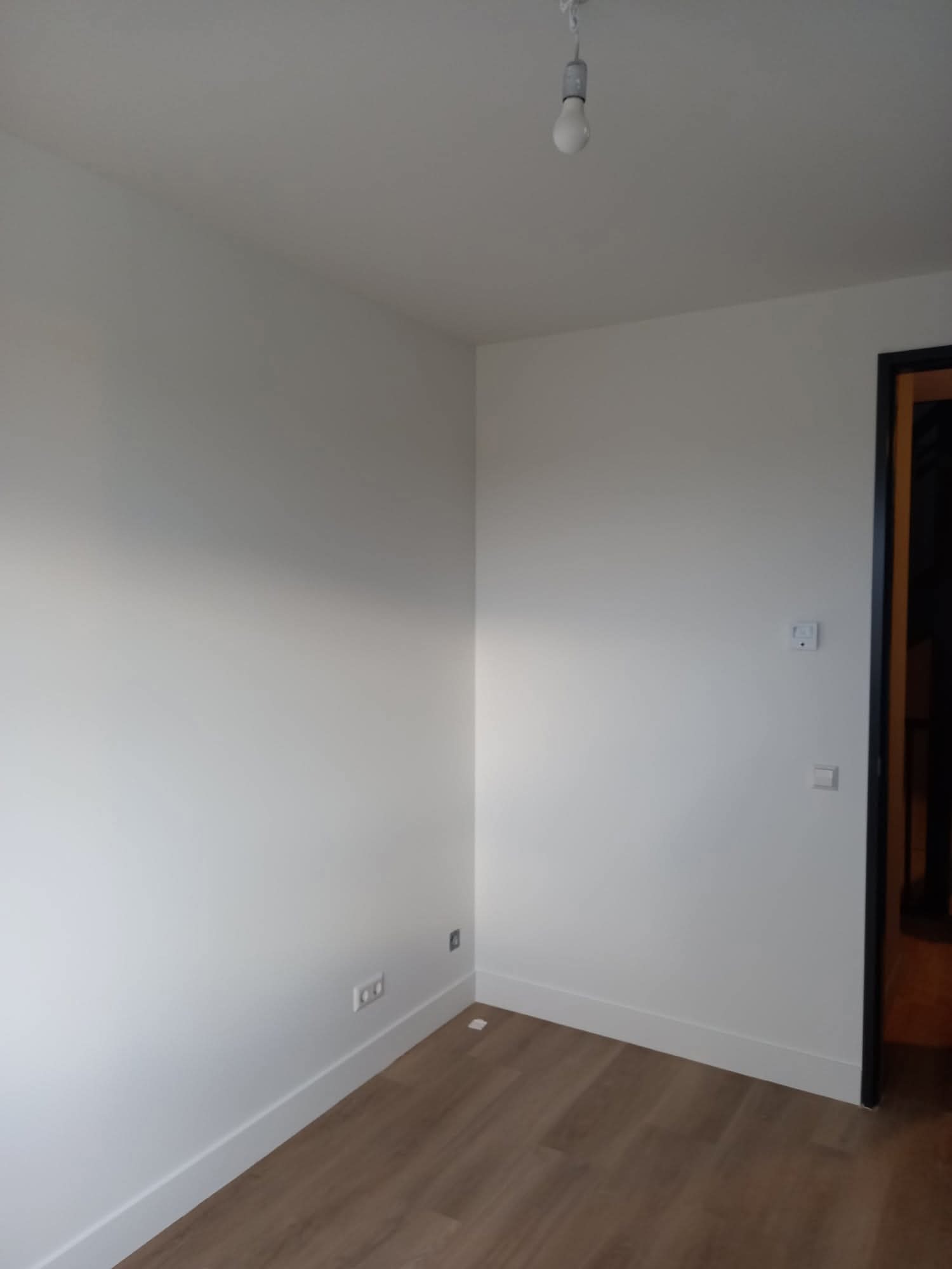 Pomalowane na biało wnętrze pokoju z panelami podłogowymi, widoczne gniazdka i włączniki. Minimalistyczny design, świeżo po malowaniu.