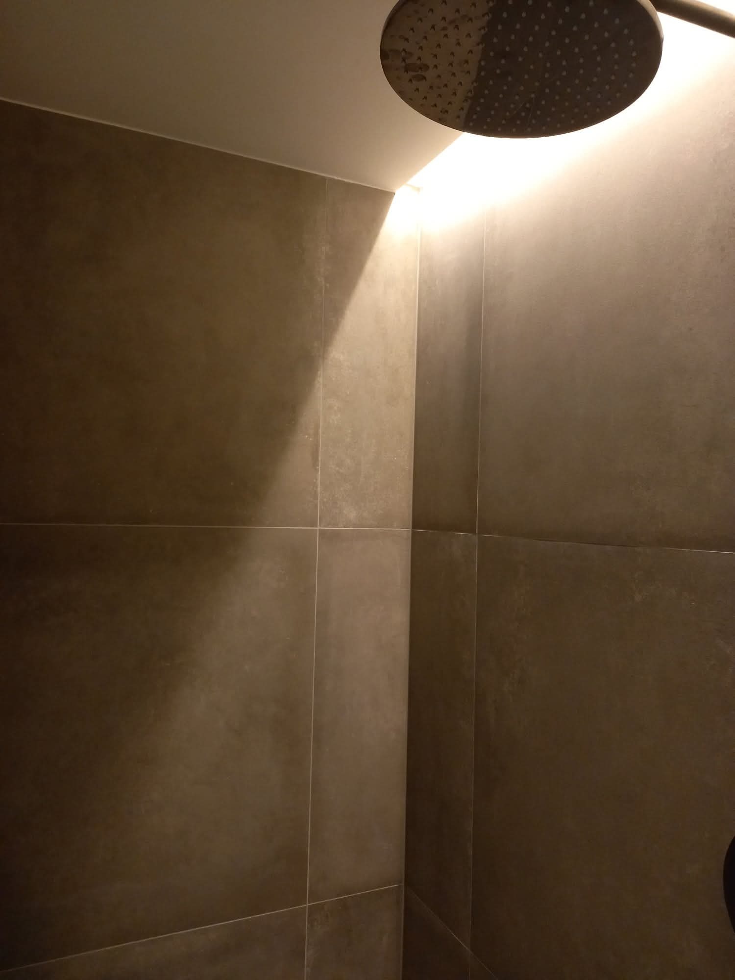 Nowoczesna kabina prysznicowa z ciemnymi, matowymi płytkami i oświetleniem LED. Widoczna deszczownica i minimalistyczne wykończenie.