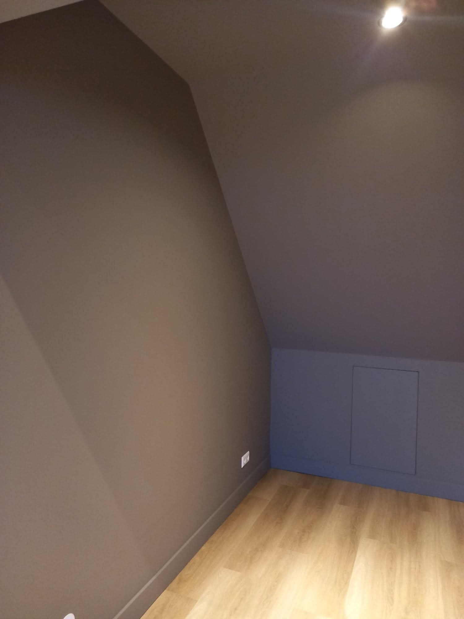 Pomieszczenie na poddaszu po malowaniu ścian na szaro i ułożeniu paneli podłogowych. Widoczny fragment ściany ze skosem i małe drzwiczki rewizyjne.