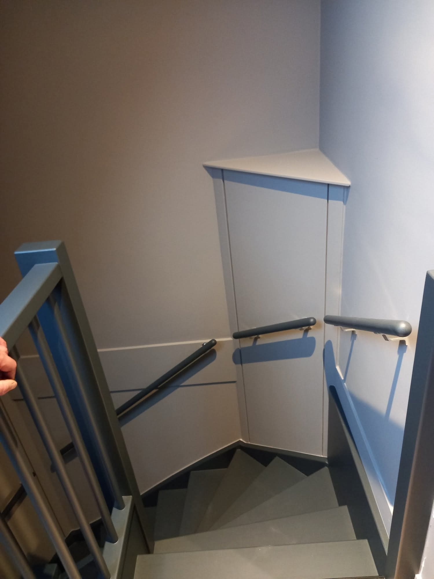 Nowoczesne schody w odcieniach szarości z minimalistyczną balustradą i oświetleniem ściennym. Widok z góry na stopnie i geometryczne detale wykończenia.